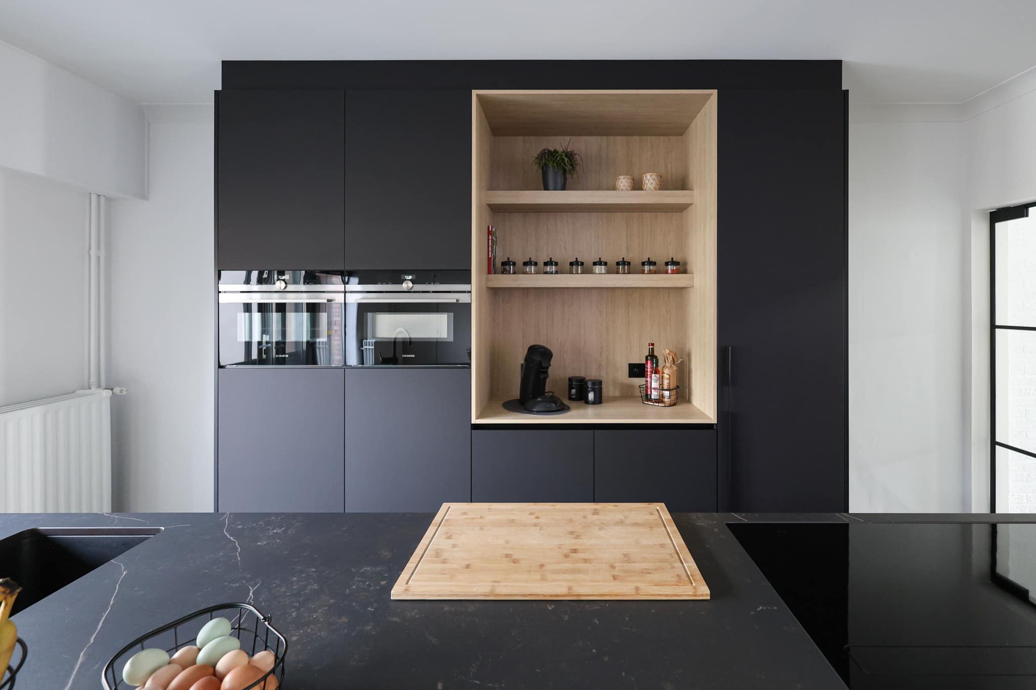 moderne zwarte keuken van JM Interieur. met lichte houten open koffiekast en een kookeiland met werkblad in graniet